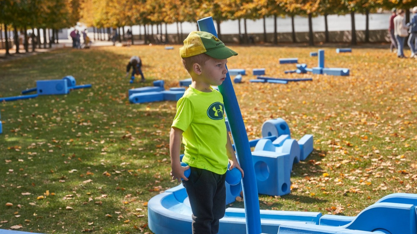A small child plays with the large, blue Imagination Playground building blocks on the FDR Four Freedoms State Park lawn
