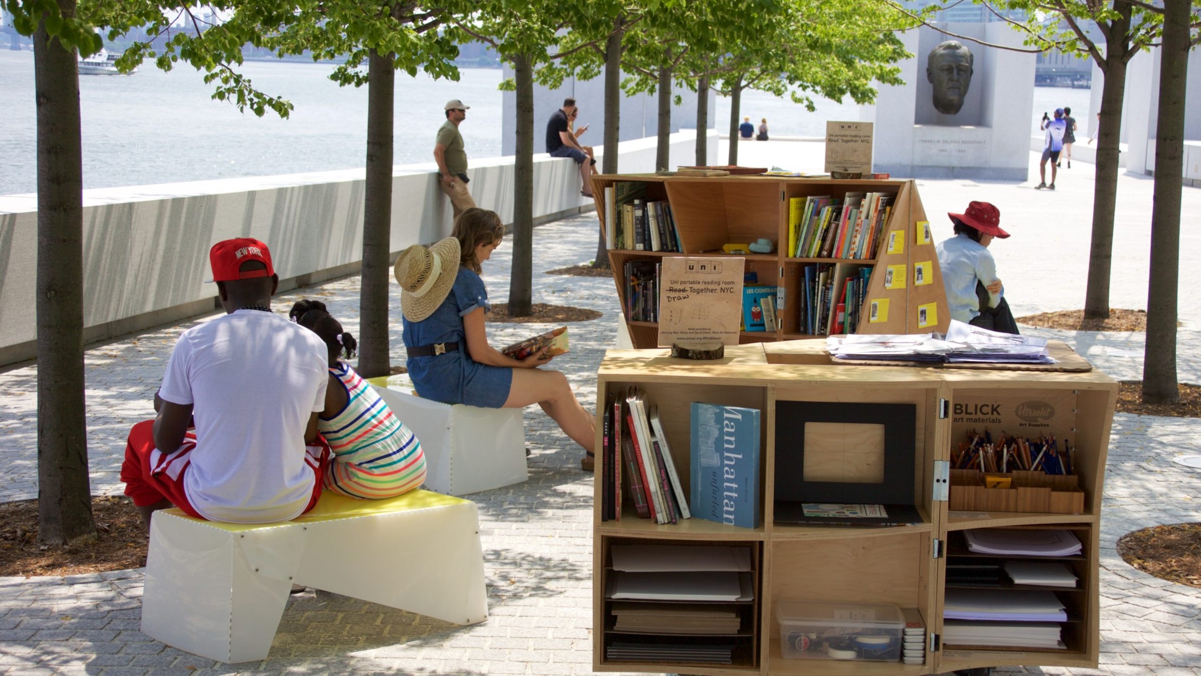 Park visitors reading books from the pop up library under the little leaf linden trees surrounded by bookshelves